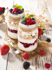 Tasty yoghurts with muesli, fresh berries and jam on wooden table. Healthy breakfast.