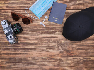Travel accessories set on wooden background: face mask. bluetooth headphones. passport. cap....