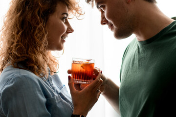 handsome man and woman stand close together and hold one glass with cocktail.