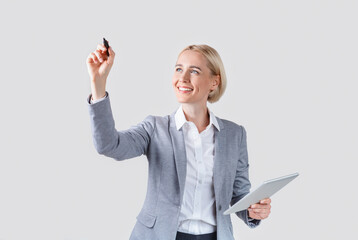 Happy businesswoman drawing or writing something on virtual screen against grey background, space...