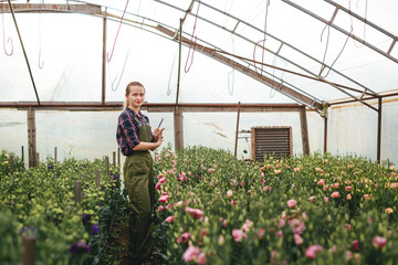 Gardener woman working on flowers in greenhouse  and makes notes. Floral business concept.