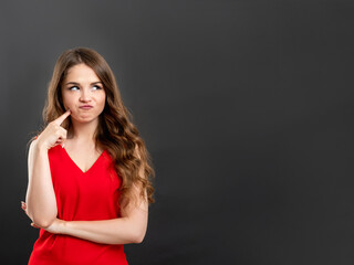 Doubtful woman portrait. Commercial background. Confused lady in red thinking isolated on gray copy space.