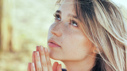 A young blonde 18 year old girl prays with folded hands.