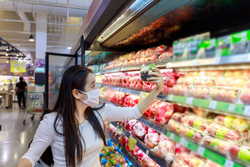 Asian woman wear face mask push shopping cart in suppermarket departmentstore. Girl, looking grocery to buy  fruit. Women wearing protective face mask hold shopping cart New normal after covid-19.
