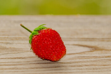 one strawberry on a wooden table with green bokeh