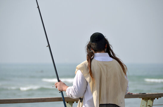Jewish man with tzitzit fishing at the sea