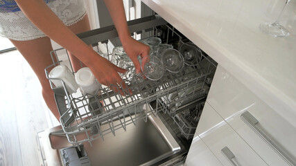 Woman washing dishes in dishwasher. Close up shot of female hands taking out clean glasses from dishwasher machine. Modern equipment for your kitchen.