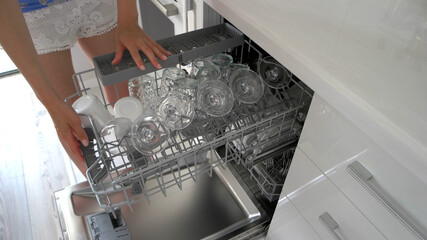 Young woman using dishwasher in the kitchen. Housewife doing home chores. Dishwasher after cleaning...