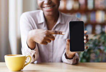 Closeup of black girl pointing at empty mobile phone screen with space for your design at city cafe