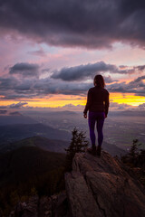 Obraz premium Adventurous Girl on top of a Rocky Mountain overlooking the beautiful Canadian Nature Landscape during a dramatic Sunset. Taken in Chilliwack, East of Vancouver, British Columbia, Canada.