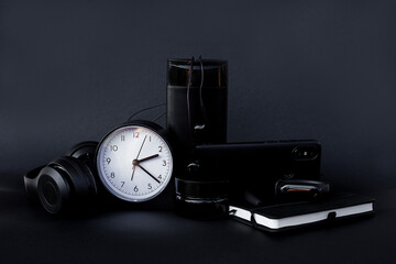 Black business accessories on a black background. Stationery. Watch, notebook, mobile, headphones, pen.