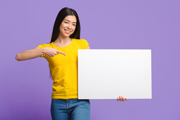 Fototapeta na wymiar Place For Your Ad. Smiling Asian Girl Pointing At White Blank Placard