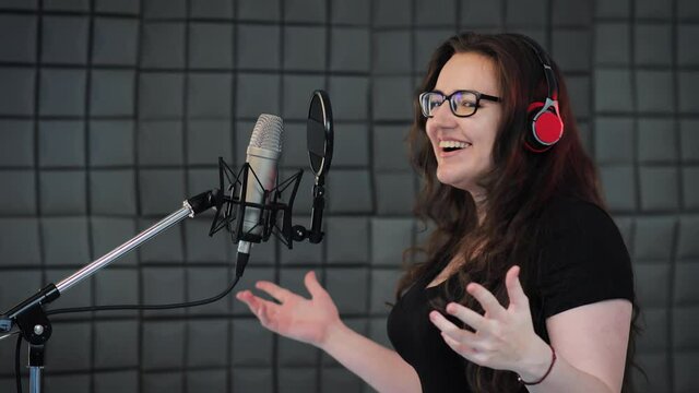 Female person records POP song at the recording studio. Singer emotionally gesturing with her hands. Soundproof room for professional recording vocal
