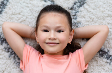 Adorable Kid Girl Smiling Lying On Floor Indoors, Above View