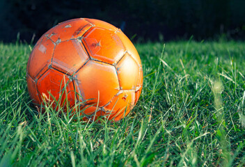 Fototapeta premium Orange soccer ball on green grass. The concept of street football. An old ball with cracks. Healthy lifestyle. Sport. Victory.