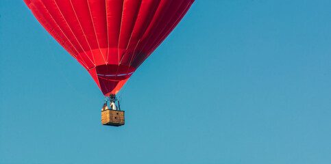 Fototapeta premium Red balloon in the sky. Aerostat. People in the basket. Fun. Summer entertainment. Romantic adventures. Modern toned photo.