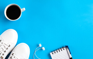 Fitness concept. Sport flat lay with white sneakers, white earphones, notebook with pen andcoffee...