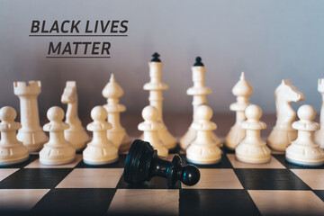 Defeated black chess pawn on a chessboard.Blurred white chess pieces in the background.Inscription...