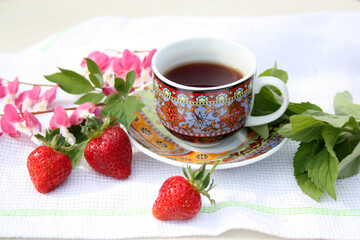 Cup of coffee on a table with pink flowers. Breakfast in the fresh air.
Horizontal photo.