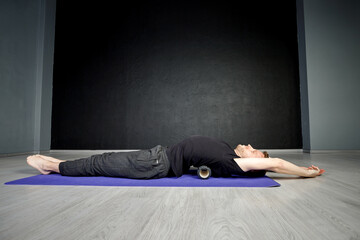 Young athletic man is working out his spine muscles with a roller.