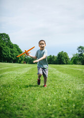 Joyful little boy runs in hands with an airplane in a field in summer.