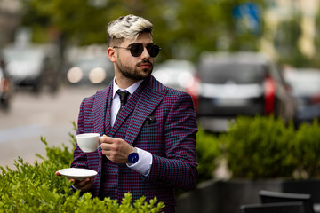 photo of man at the cafe wearing on violet luxery three-piece suit drinking coffee or tea from cup
