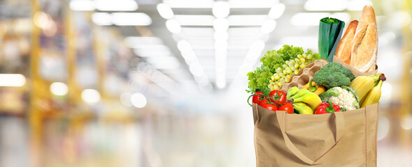 Eco-friendly reusable shopping bag filled with different fruits, vegetables and bread. Supermarket blur background.