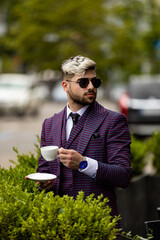 Fototapeta premium photo of man at the cafe wearing on violet luxery three-piece suit drinking coffee or tea from cup