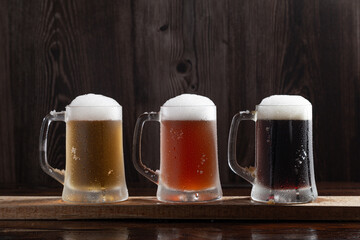 Three kinds of cold beer in jugs on  wooden base.