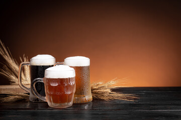 Three kinds of cold beer in jugs and wheat spikes on  wood base.