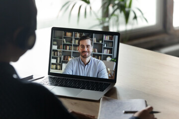 Girl trainee learn language wear headphones view over her shoulder laptop screen where male tutor share knowledge smile looks at camera. Colleagues work distantly using video call and computer concept