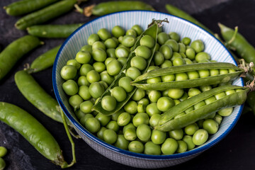 young  green peeled peas in a bowl on black background