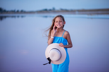 girl in a hat on the beach. Beautiful long-haired girl at sunset in the pink-legged lake. Travels. Nature and beaches. Child portrait

