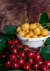 Naklejka na ściany i meble White plate with ripe yellow and red cherries. Fresh sweet cherry with leaves and drops of water. Closeup of fresh ripe sweet yellow and red cherries. Wood background