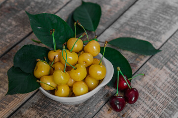 Red and yellow cherries. Contrast of colors. Fresh ripe sweet cherries in a white plate on a wooden background. Close-up