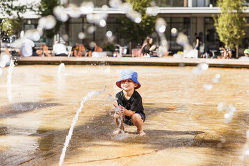 Little boy playing with water jet in fountain