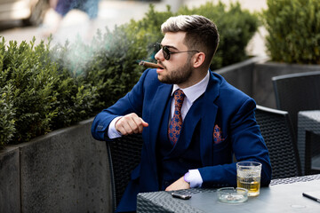 Stylish handsome man smoking cigar and drinking whiskey at a cafe
