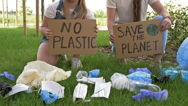 Two young women squatting near a pile of garbage with posters SAVE THE PLANET and NO PLASTIC. Tons of garbage was added during the COVID-19 pandemic.
