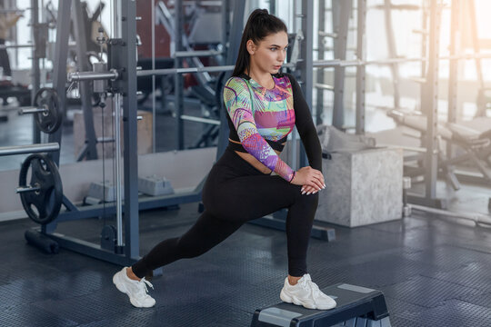 Attractive millennial lady stretching on step platform at fitness club