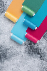 Colorful threads on bobbins and samples of colored fabrics, sewing kit. On a gray concrete background. Place for tex