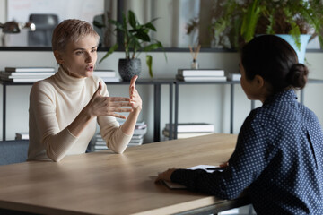 Diverse business women sit in front of each other conduct business conversation. Job interview applicant and headhunter talk. Company representative make offer to client convince buy services concept - obrazy, fototapety, plakaty