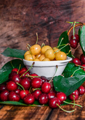 Yellow and red cherries with drops of water. Beautiful, ripe sweet cherries with leaves on a wooden background.