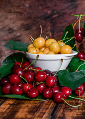 Yellow and red cherries with drops of water. Beautiful, ripe sweet cherries with leaves on a wooden background.