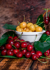 Yellow and red cherries with drops of water. Beautiful, ripe sweet cherries with leaves on a wooden background.