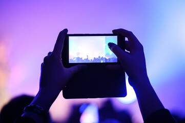 hands from the crowd take videos and photos on a smartphone as a keepsake of a music festival. blurred background. atmosphere of a musical concert - Powered by Adobe