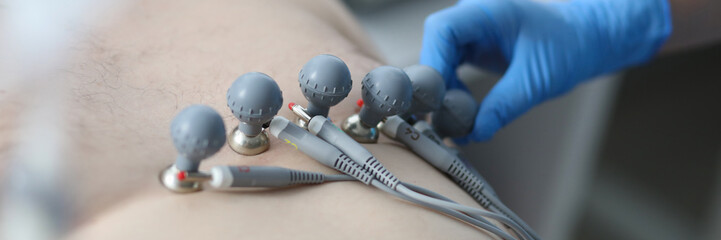 Close-up of clinical worker stick special equipment to mans chest for ecg test. Macro shot of patient under medical care. Cardiology appointment and medicine concept