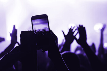 hands from the crowd with a can shoot video on a smartphone as a keepsake of a music festival. blurred background. atmosphere of a musical concert