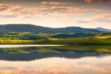 Green muntains at sunset and their reflections in the lake. Beautiful summer landscape. South Ural, Russia