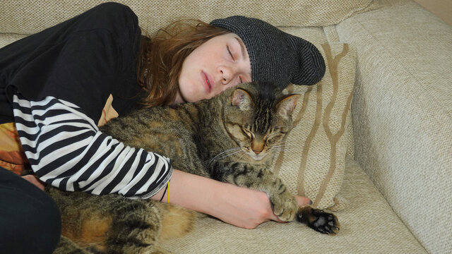 Teenage girl napping on couch while hugging her cat
