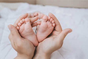 The legs of a small child sleeping on a white bed in the arms of his beloved mother close-up. Woman's happiness. Photography, concept.